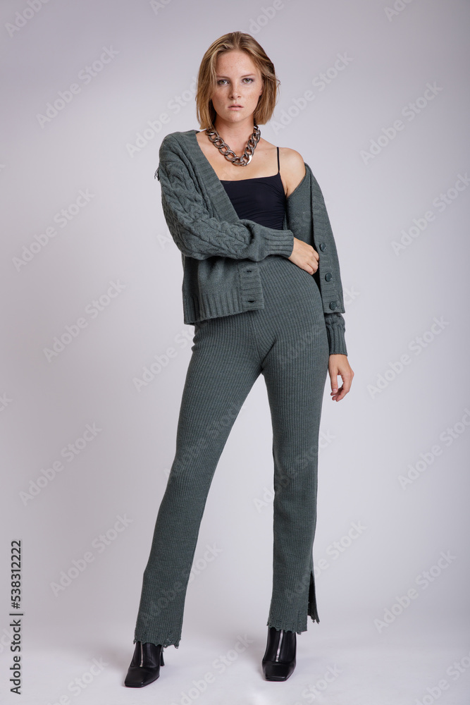High fashion photo of a beautiful elegant young woman in a pretty green knitwear sweater, pants, trousers black top posing over white, soft gray background. Studio Shot, portrait. High fashion photo of a beautiful elegant young woman in a pretty green knitwear sweater, pants, trousers black top posing over white, soft gray background. Studio Shot, portrait.