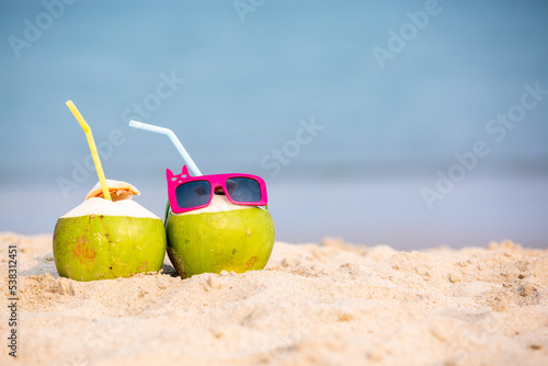 Tropical summer vacation family holiday, Coconut wearing stylish sunglasses on the sand beach with sea background, Sunny day on the beach tropical island, summer tropical pineapple.