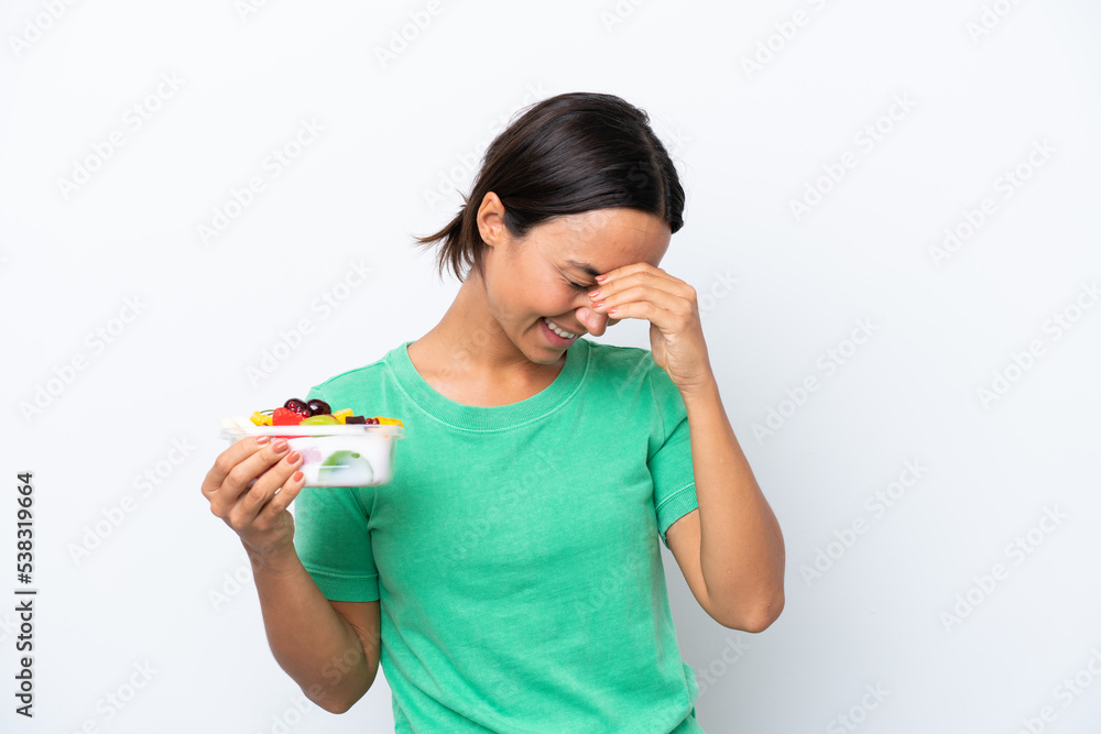 Young hispanic woman holding a bowl of fruit isolated on white background laughing Young hispanic woman holding a bowl of fruit isolated on white background laughing