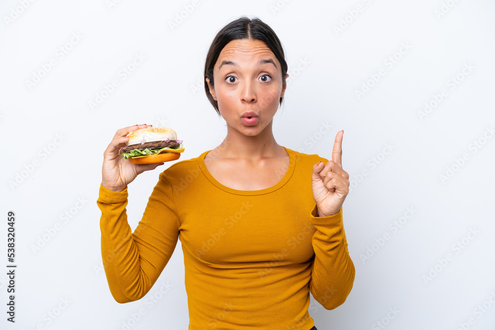 Young hispanic woman holding a burger isolated on white background intending to realizes the solution while lifting a finger up Young hispanic woman holding a burger isolated on white background intending to realizes the solution while lifting a finger up