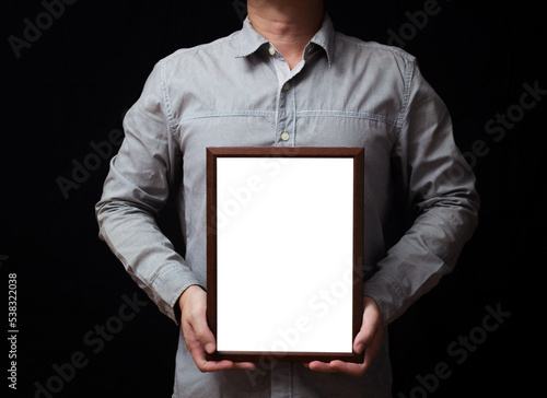 A blank diploma or a mockup certificate in the hand of a man employee wearing shirt on black background. The vertical picture frame is empty and the copy space.