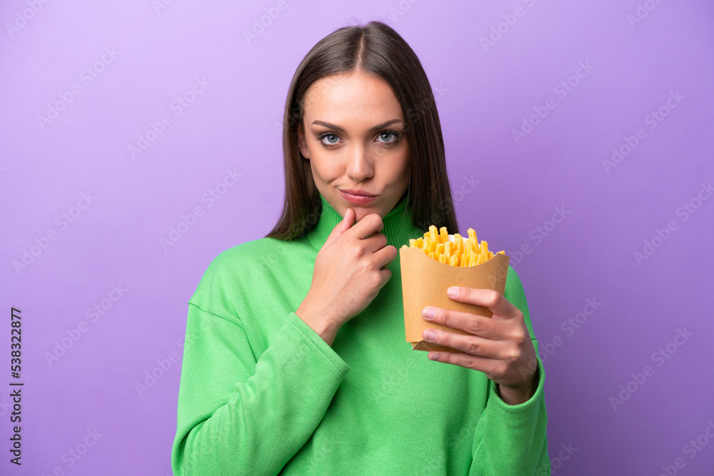 Young caucasian woman holding fried chips on purple background thinking Young caucasian woman holding fried chips on purple background thinking