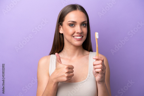 Young caucasian woman brushing teeth isolated on purple background with thumbs up because something good has happened