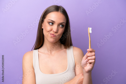 Young caucasian woman brushing teeth isolated on purple background with sad expression