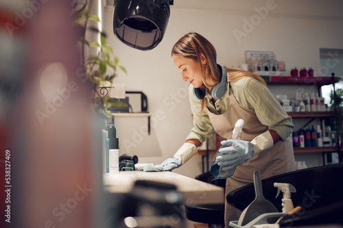 Hair salon, cleaner and woman cleaning a workplace in Australia with equipment to disinfect. Housekeeper, maid or girl dusting table with hygiene, detergent and sanitizing products in beauty parlor