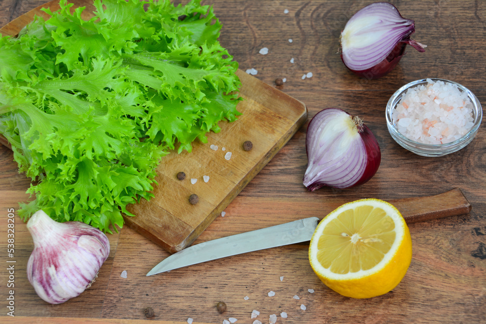green salad leaves on cutting board with knife, red onion, garlic and lemon green salad leaves on cutting board with knife, red onion, garlic and lemon