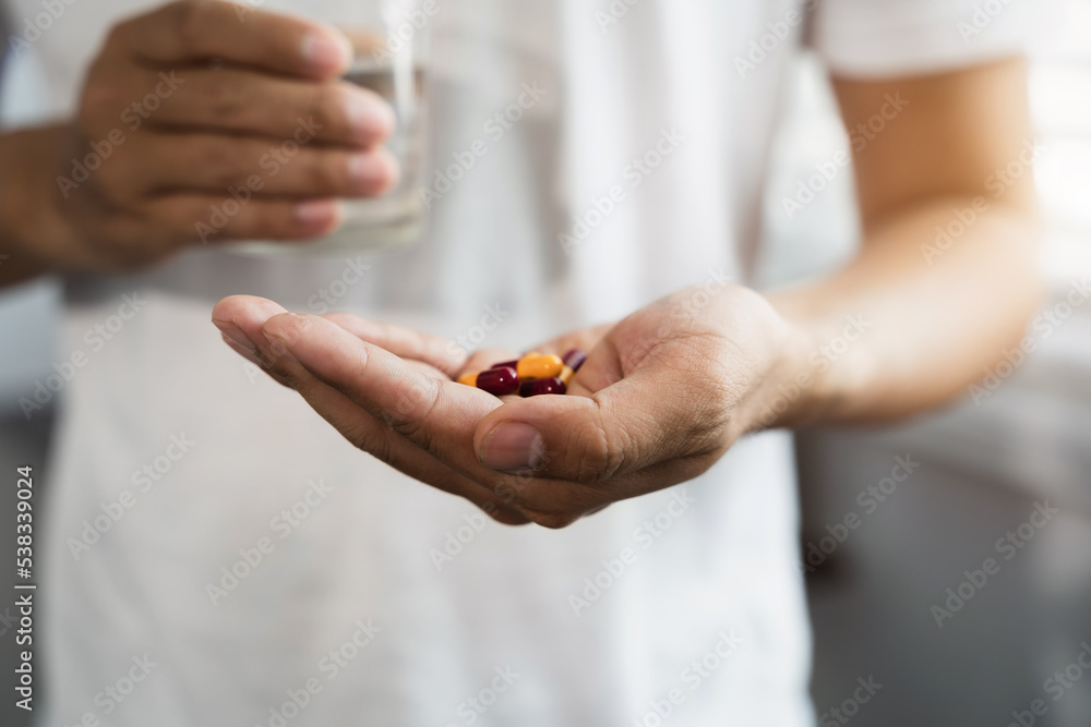 male hand holding pills and glass of water male taking pills Discomfort health care concept. male hand holding pills and glass of water male taking pills Discomfort health care concept.