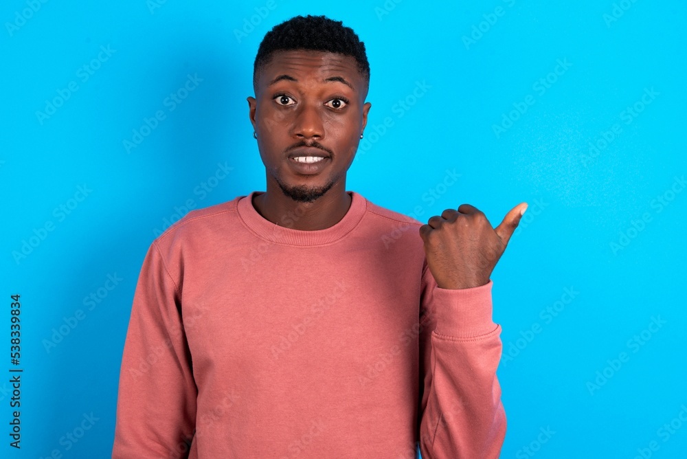 Lovely young handsome man wearing pink sweater over blue background pointing aside with forefinger, showing at copy space having news about bargains