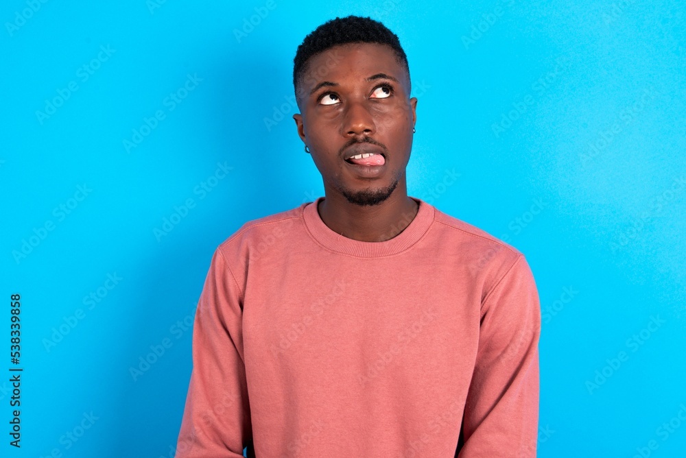 young handsome man wearing pink sweater over blue background showing grimace face crossing eyes and showing tongue. Being funny and crazy young handsome man wearing pink sweater over blue background showing grimace face crossing eyes and showing tongue. Being funny and crazy