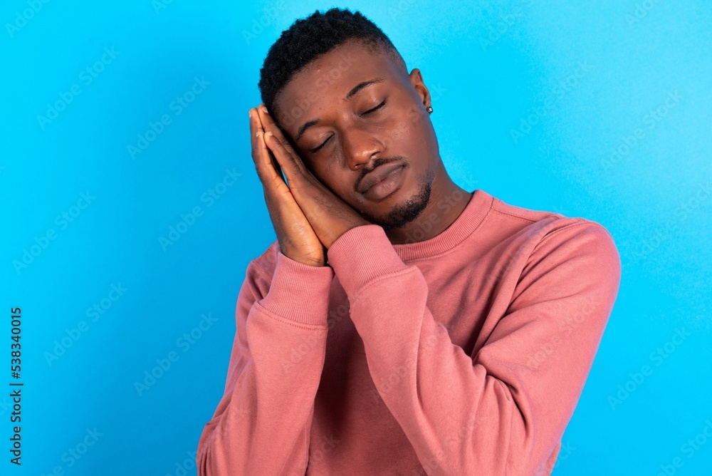 young handsome man wearing pink sweater over blue background sleeping tired dreaming and posing with hands together while smiling with closed eyes. young handsome man wearing pink sweater over blue background sleeping tired dreaming and posing with hands together while smiling with closed eyes.