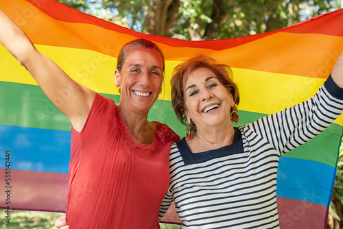 A middle-aged girl next to an older lady raising the gay rainbow flag. Support for the lgbti+, gay, homosexual, bisexual, lesbian, trans, non-binary community. Fight for the freedom and rights