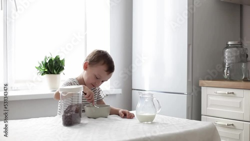 a cute little boy is stirring chocolate flakes with milk with a spoon and eating them. the concept of healthy nutrition.