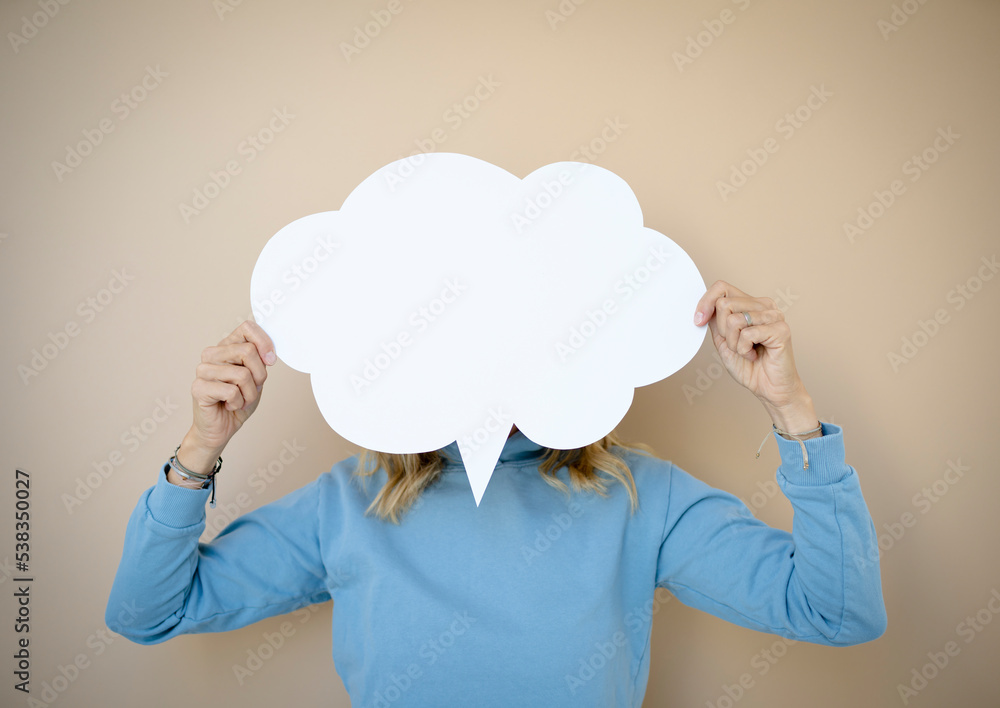 beautiful young woman with curly blond hair stands in front of brown wall and holds white speech bubble, thought bubble beautiful young woman with curly blond hair stands in front of brown wall and holds white speech bubble, thought bubble