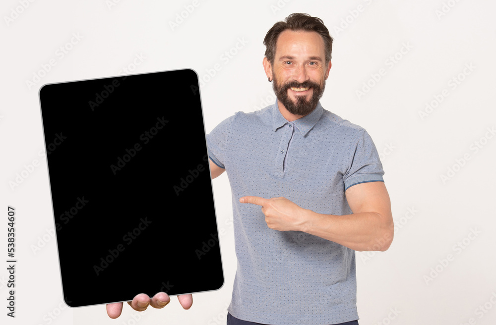 Bearded happy smiling man pointing to black mock-up screen of big tablet pc holding in hand isolated over white background and looking at camera Bearded happy smiling man pointing to black mock-up screen of big tablet pc holding in hand isolated over white background and looking at camera