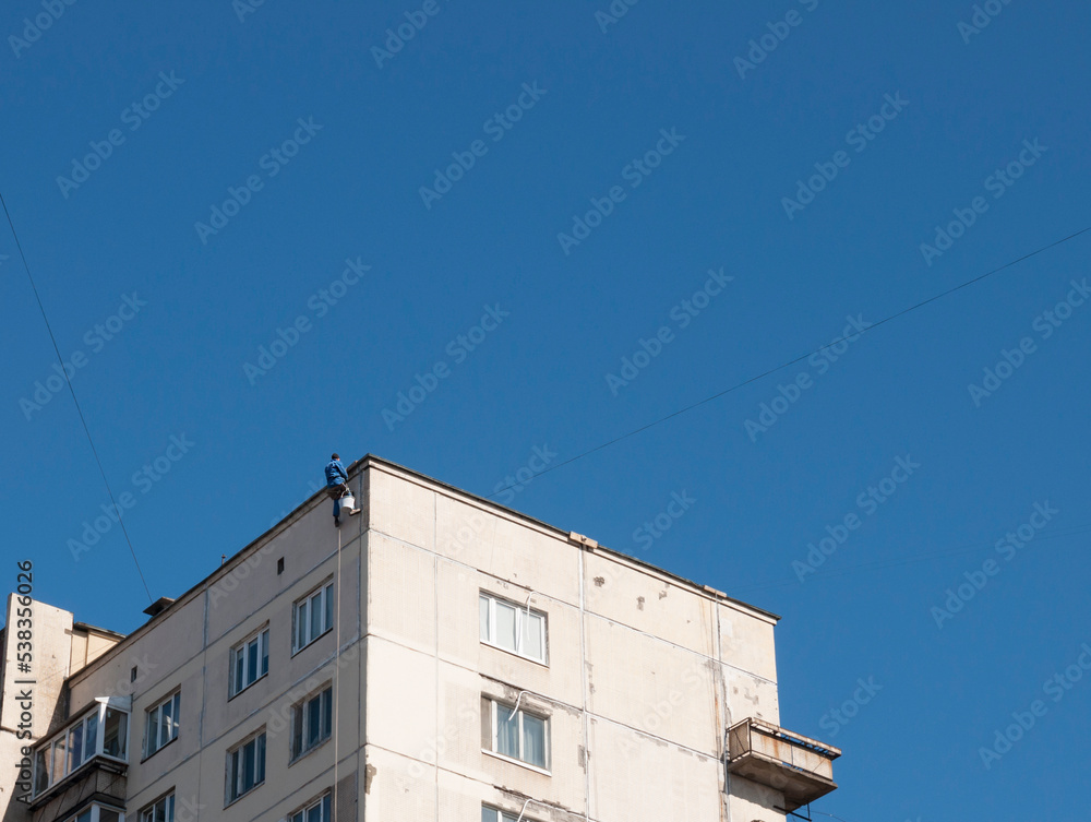 A working industrial climber hangs from the roof of the house sealing the seams between the panels