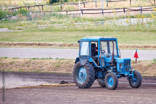 A blue tractor levels the dirt road, kicking up a cloud of dust behind. copy space.