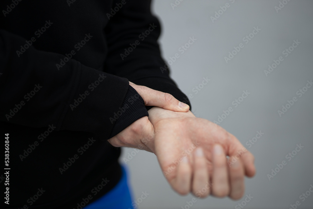 Fototapeta premium A male athlete in a hoodie and thermal underwear checks the pulse on his hand. Heart rate control close-up on a gray background.