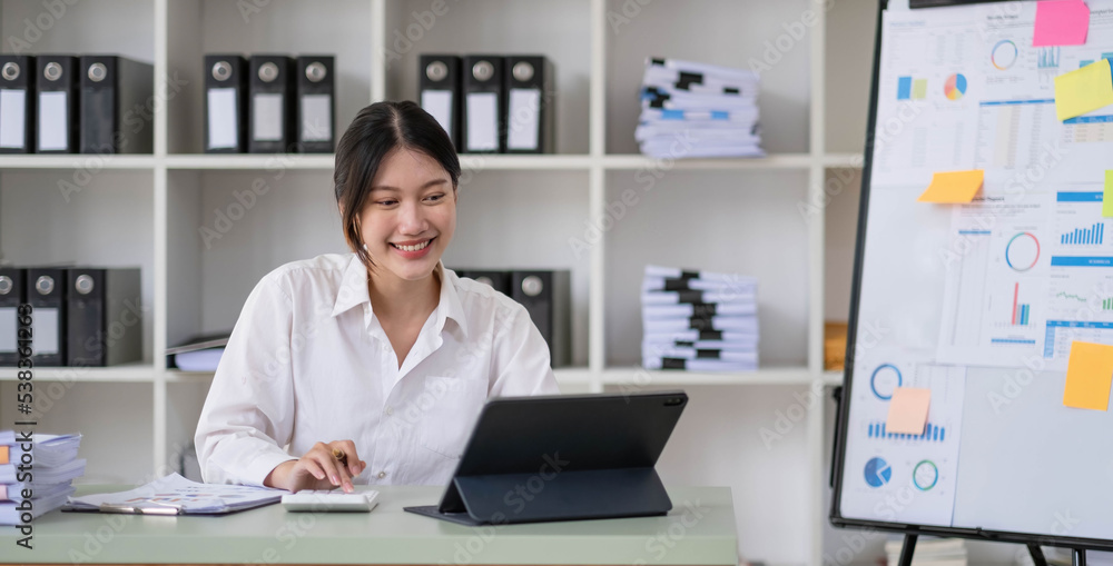 Asian Businesswoman Using laptop computer and working at office with calculator document on desk, doing planning analyzing the financial report, business plan investment, finance analysis concept.