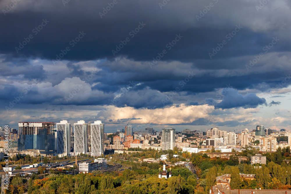 Thunderclouds over the city illuminated by the rays of the evening sun. Beautiful cityscape from a bird's eye view. Thunderclouds over the city illuminated by the rays of the evening sun. Beautiful cityscape from a bird's eye view.