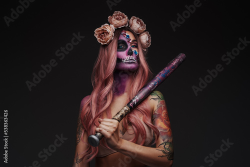 Studio shot of attractive female model with makeup and wreath of roses holding club.