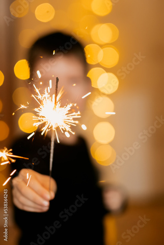 fireworks close-up in the hands of a child, against the background of a yellow Christmas garland. Happy child with sparklers on New Years celebration