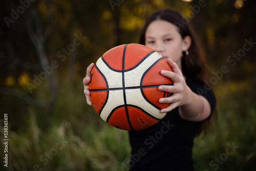 Teen girl holding out ball outside - play together concept photo