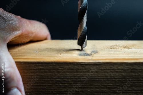 Close up of drill bit drilling into wood. Joinery and construction work close up. Wood chippings fly off a metal drill. Handyman bores holes into a wooden board.  Detailed drill.