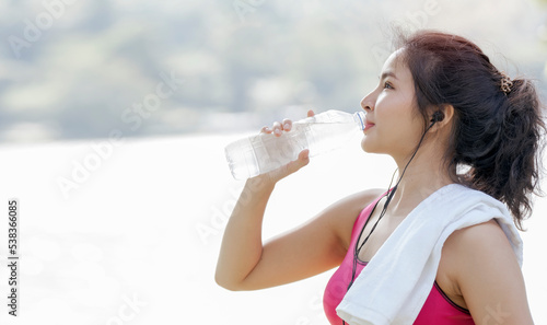 Beautiful asian sportswoman drinking water after workout or exercise outdoors, copy space.