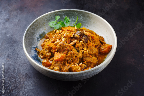 Traditional Indian vegetarian Madras curry stew with sweet potatoes and roasted cashew nuts served as close-up in a grey Nordic design bowl with copy space