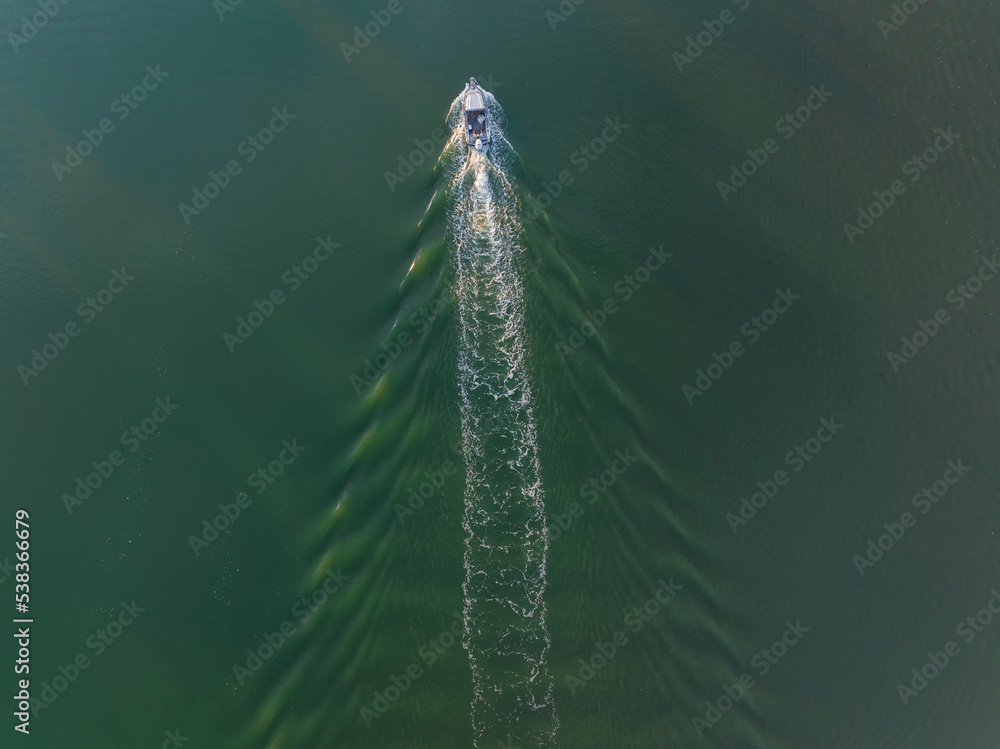Aerial view of a small boat creating a wake in a wide river Aerial view of a small boat creating a wake in a wide river