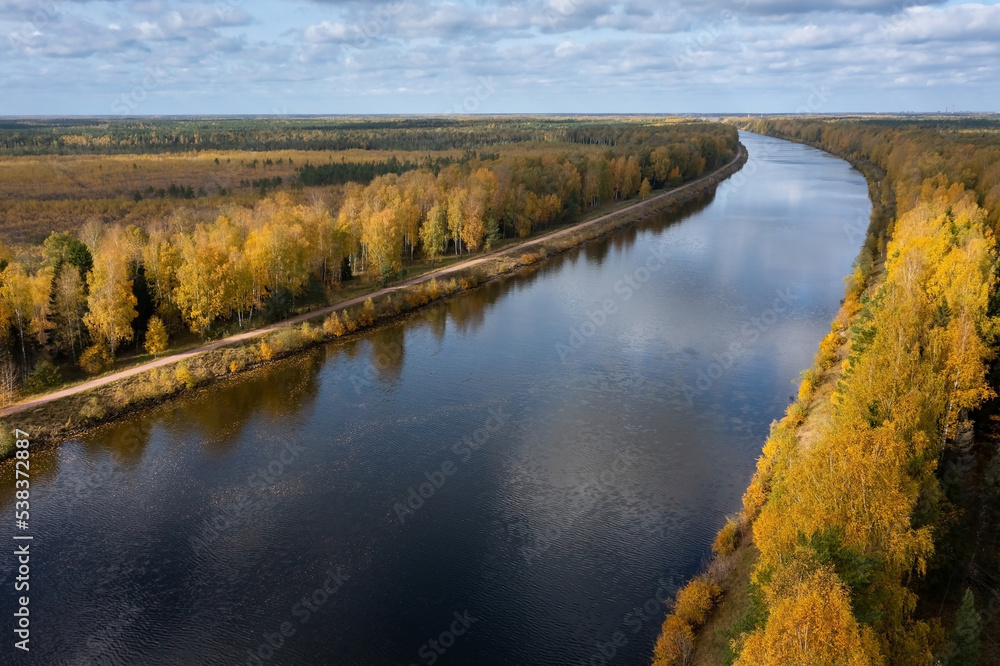 Aerial panoramic view of a long canal leading through a forest in autumn colors, Dubna, Russia