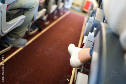 Action of an airplane passenger is crossing legged sitting at the economy class, with narrow corridor as blur background. People in transportation action, close-up and selective focus at heel part. © Nattawit