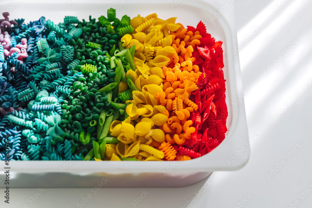 Sensory bin with dried pasta in rainbow colors. Dyed pasta for play and