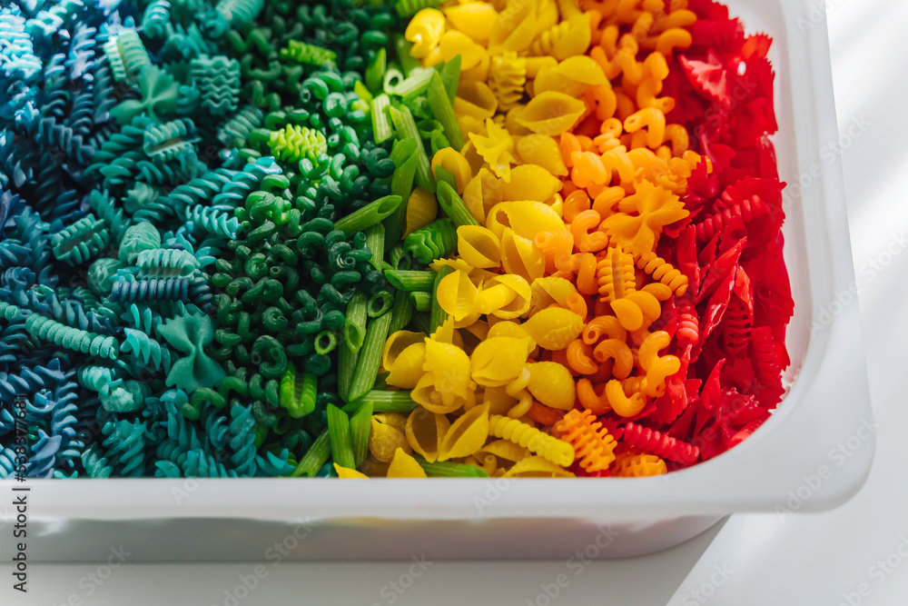 Sensory bin with dried pasta in rainbow colors. Dyed pasta for play and