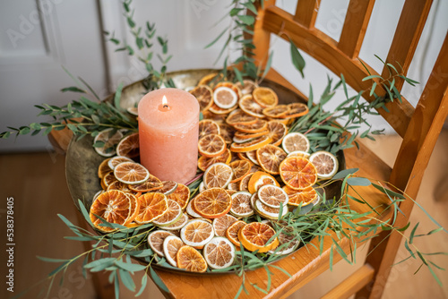 Adventsschale mit Kerze, Eukalyptus und getrockneten Orangenscheiben auf goldenem Teller dekoriert für Weihnachten, minimalistische Dekoration
