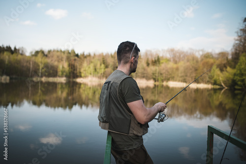 A young man in a vest is fishing on a small pond. Catching fish in nature at sunset. A relaxing hobby.