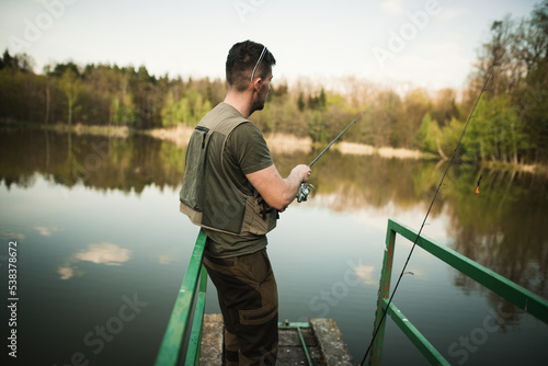 A young man in a vest is fishing on a small pond. Catching fish in nature at sunset. A relaxing hobby.