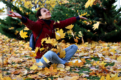 Outdoors lifestyle portrait of young woman throwing leaves in autumn park photo