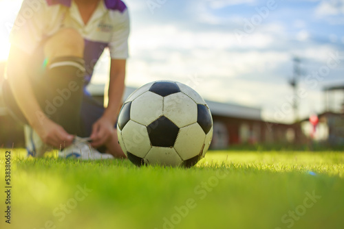 Sport man tying shoes with classic ball before playing soccer football on green grass field. Athlete sportman player and exercise concept. © nateejindakum