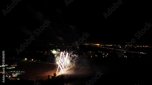 Aerial drone footage of bright firework which is fired from the beach of the river at summer night. Triathlon celebration held in Lipetsk on green island. Colorful explosion in the dusk sky over city. photo