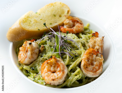 Spaghetti pesto topped with shrimps and and garlic bread.