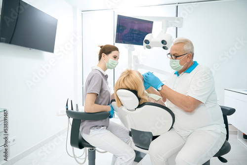 Seriously dentist is working with female patient while nurse is helping to him