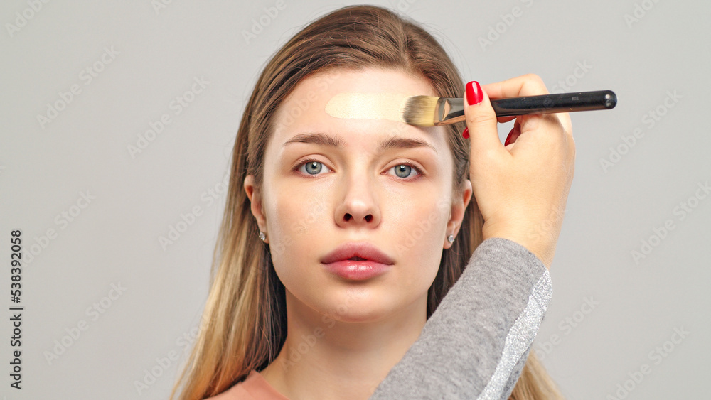 Fototapeta premium Makeup artist or stylist applies foundation or concealer to the face of the female model. Visagiste applying cosmetic foundation base on a face.