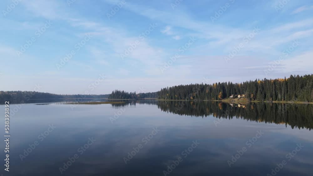 Drone flying forward just above the surface of a calm lake surrounded by a forest with cabins along the right side
Drone flying forward just above the surface of a calm lake surrounded by a forest with cabins along the right side
