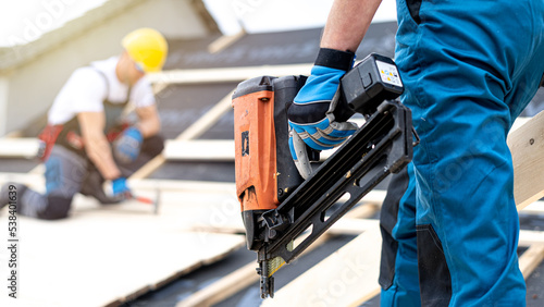 The electric nail gun in a worker hand while working on the roof. photo