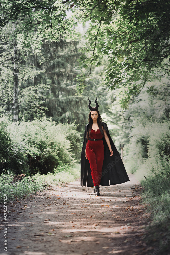 beautiful witch in a black cloak with horns Maleficent walks through the dense forest