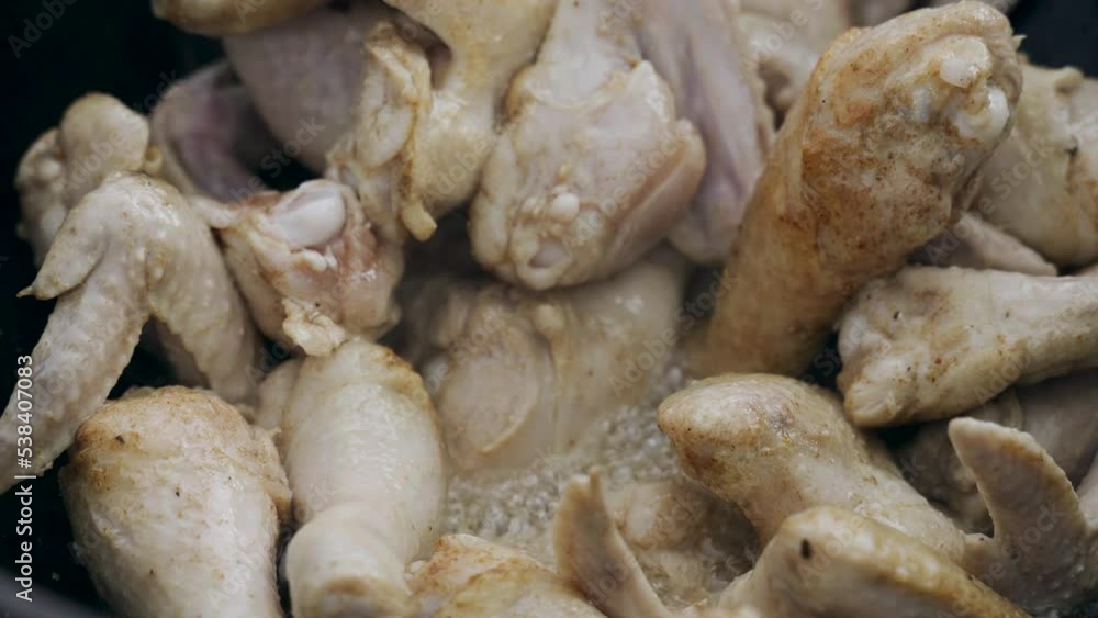 The cook prepares chicken - legs and wings in a cauldron in the open air. Close-up. The cook prepares chicken - legs and wings in a cauldron in the open air. Close-up.
