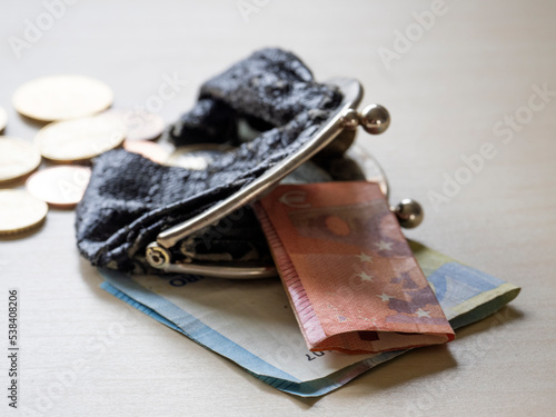 Coins spill out of a torn purse containing two 10 and 20 Euro banknotes.