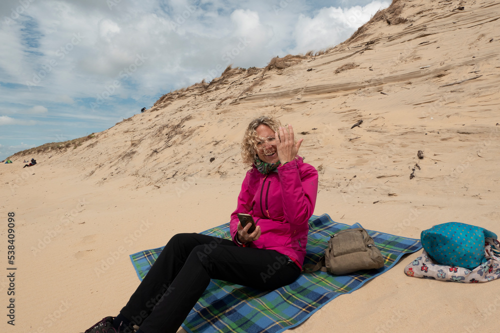 woman sitting on the beach picknik in the sand warm dressed with smartphone