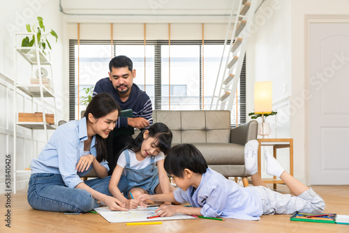 Happy Asian family relaxing on sofa while kid drawing on floor. Little boy girl having fun, friendship between siblings, family leisure time in living room at home. © anon
